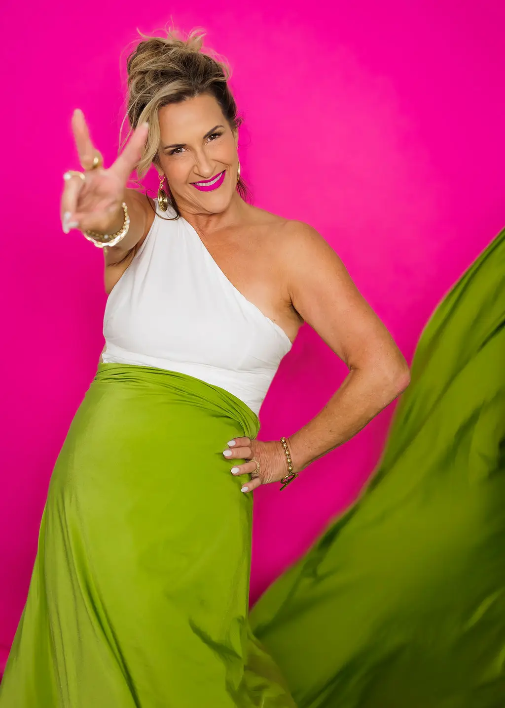 Stacey smiling and making a peace sign in a chartreuse skirt against a pink background